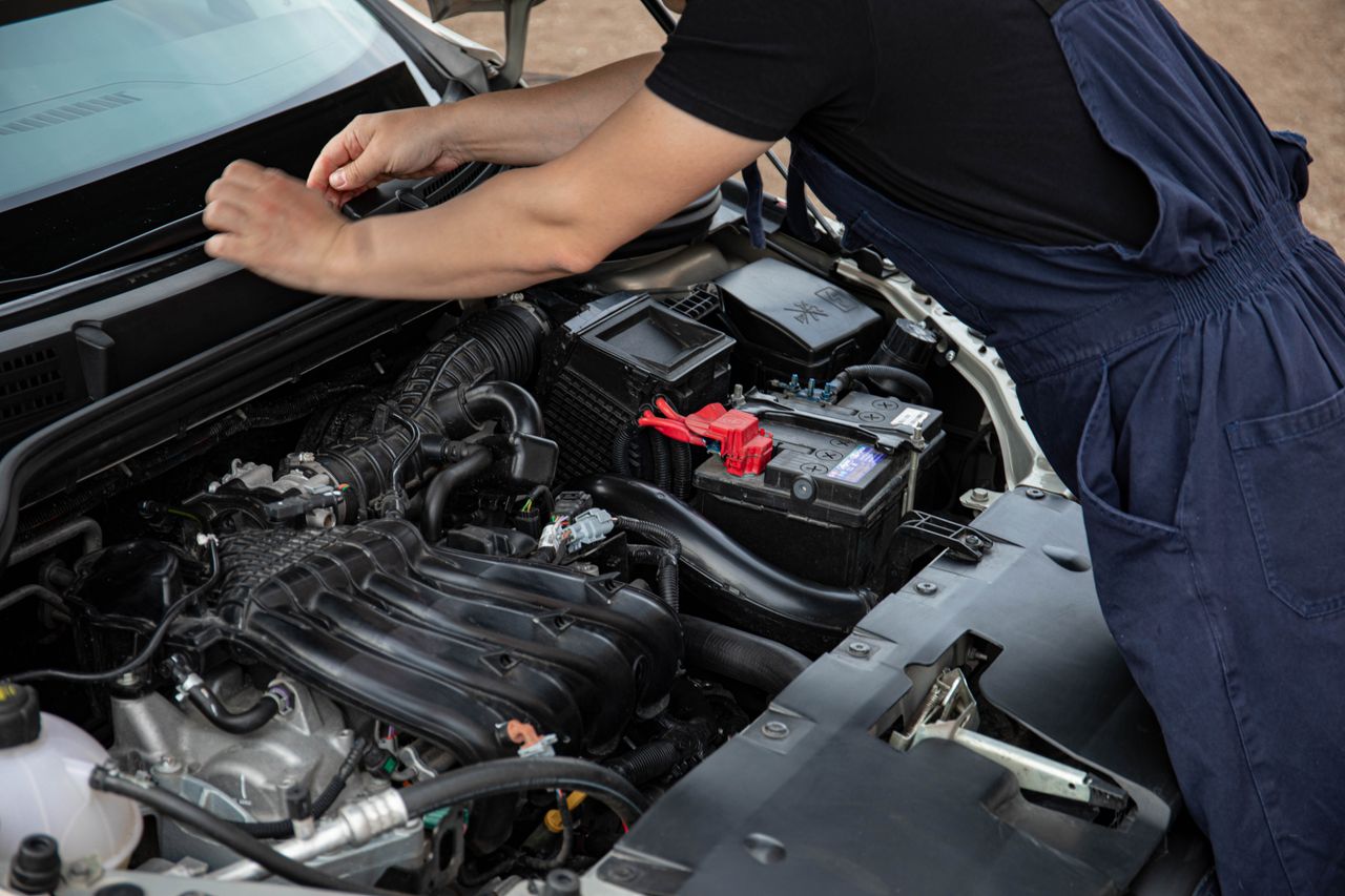 Anasayfa Mechanic performing maintenance on a car engine outdoors during the day.